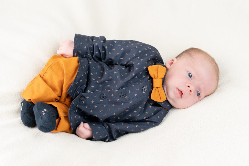 Bébé avec noeud papillon, allongé, yeux grands ouverts. Photo Studio Polidori