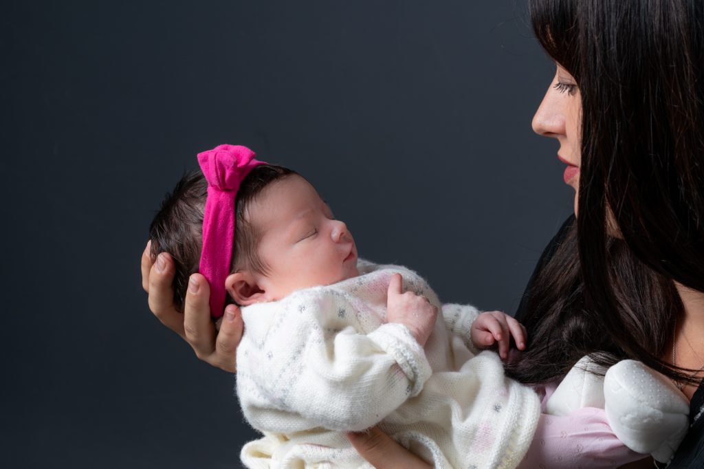 Maman regardardant son bébé endormi dans ses bras. Au studio, fond noir. Photo Studio Polidori