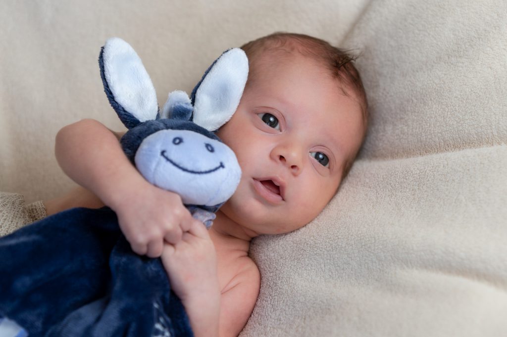 Bébé grands yeux ouverts, tenant femement son doudou. Photo Studio Polidori