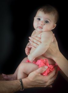 Photo de bébé, réalisé au flash, assis dans les bras de maman et papa. Photo Studio Polidori
