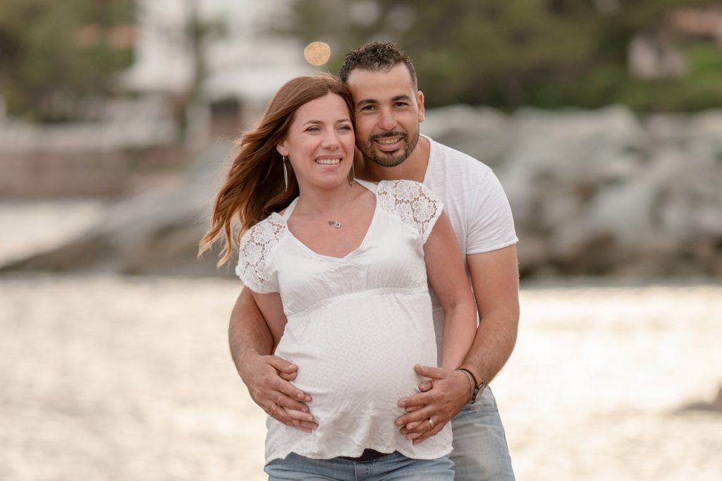 Futur papa enlaçant son épouse enceinte, au bord de mer, soleil couchant. Photo Studio Polidori