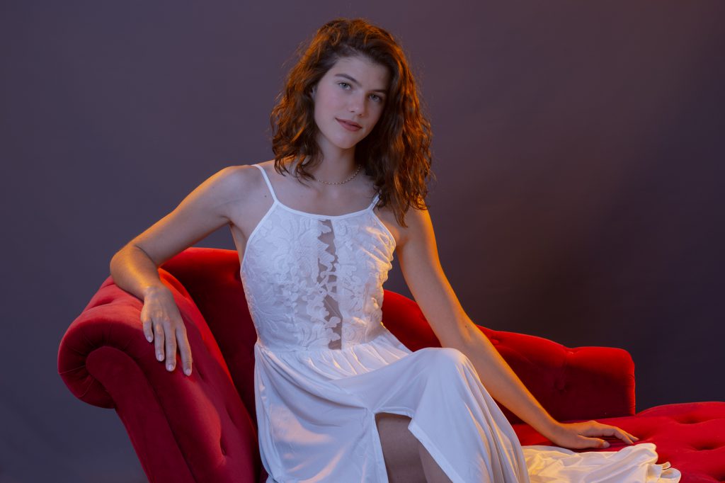 Une jeune femme , avec robe blanche, assise sur méridienne rouge. Photo Studio Polidori