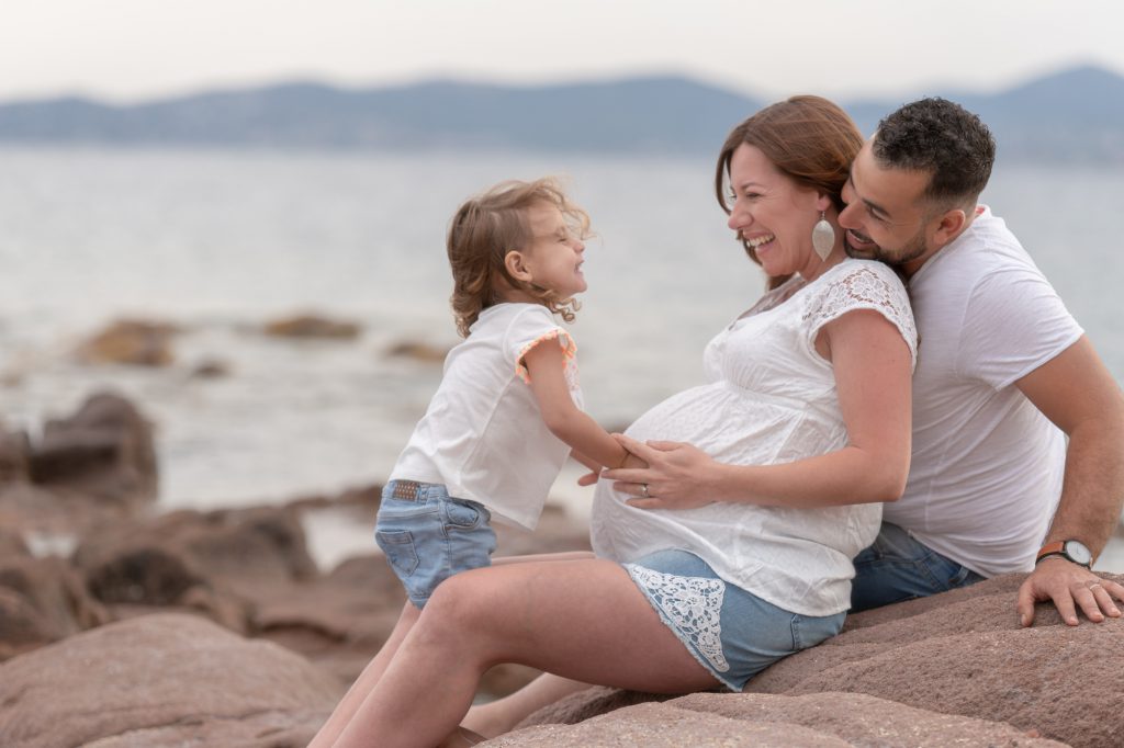 Dans les rochers en bord de mer, jeux entre femme enceinte, papa et petite fille. Photo Studio Polidori