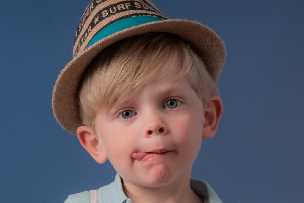 Un petit garçon avec un chapeau, fait une grimace en tirant la langue. Photo Studio Polidori