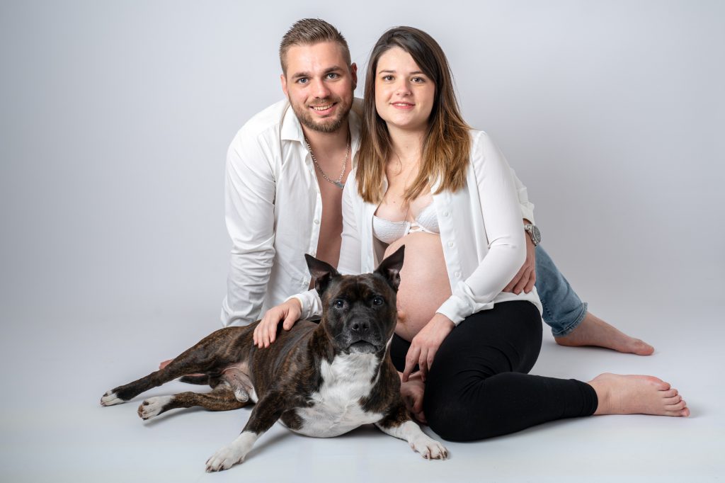 Jeune femme enceinte, et le futur papa accompagné de leur chien assis au sol. Photo Studio Polidori