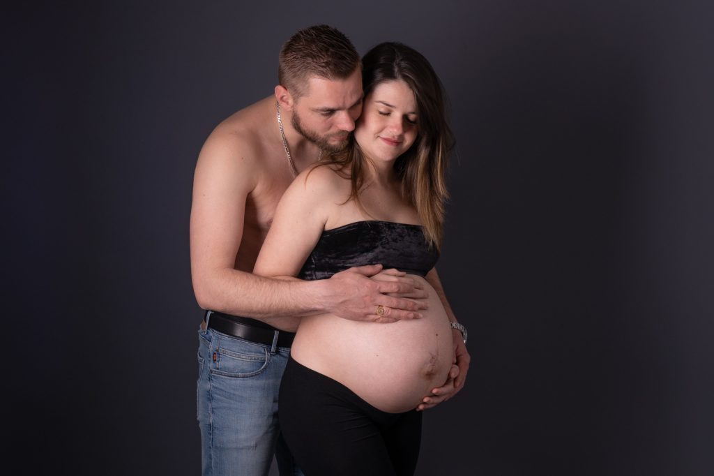 Futur parents, mains enlacés sur le ventre rond, regard tendre. Photo Studio Polidori