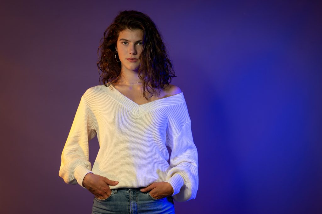 Jeune femme en pull blanc, pose cool sur fond studio dégradé violet/bleu. Photo Studio Polidori