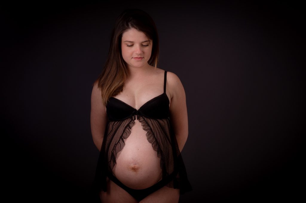 Une jeune femme enceinte, nous dévoile son ventre rond derrière nuisette.
