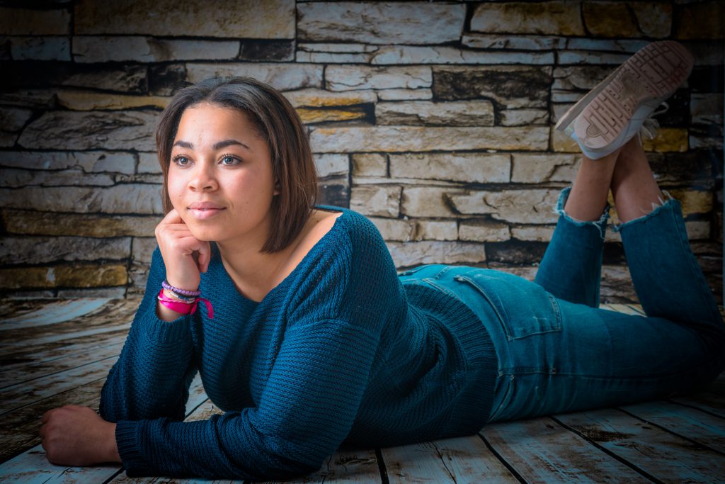 Une jeune femme pose décontractée allongée, devant mur de briques. Photo Studio Polidori