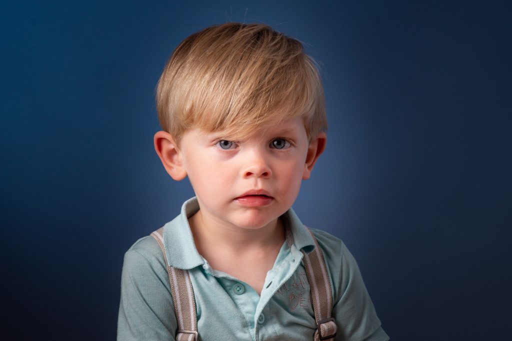 Un jeune garçon, regard attentif, au studio sur fond bleu. Photo Studio Polidori