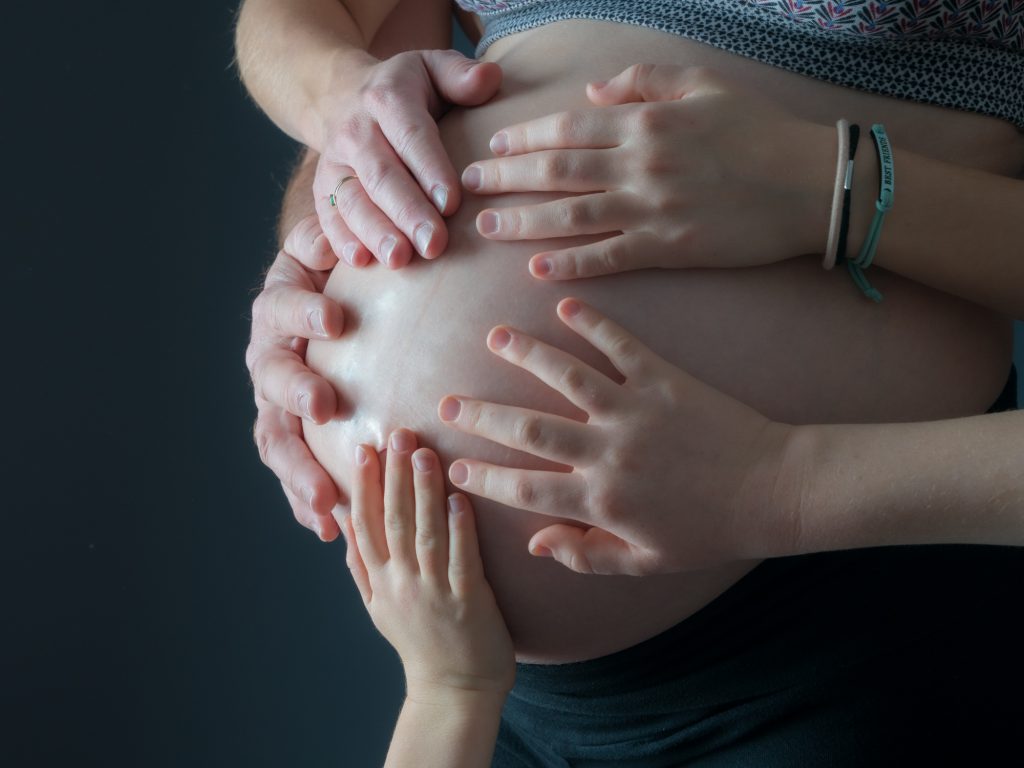 Toute la famille met une main sur le ventre rond de la maman enceinte. Photo Studio Polidori