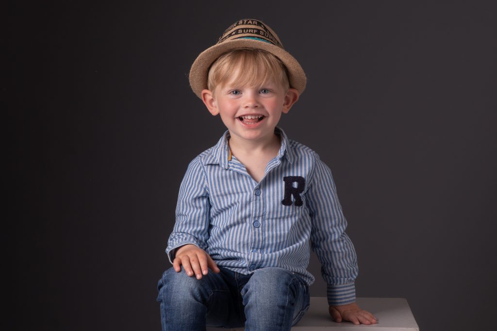 Un petit garçon, assis avec un grand sourire. Photo Studio Polidori