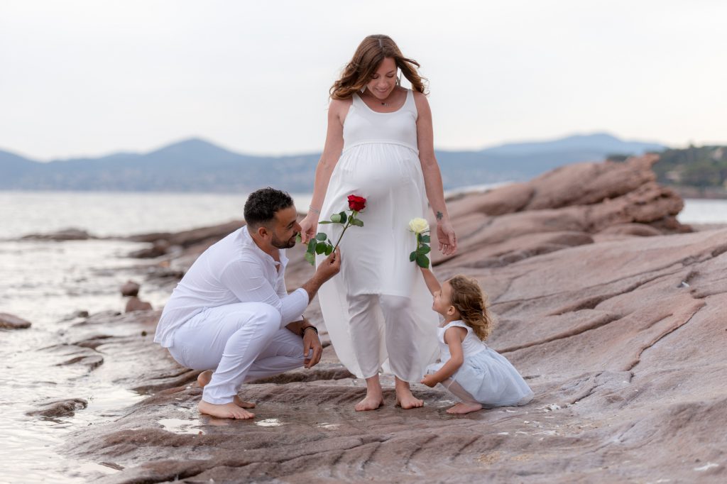 Sur les rochers au bord de mer, à Boulouris. Petit fille et papa offrent des fleurs au ventre rond de maman enceinte. Photo Studio Polidori