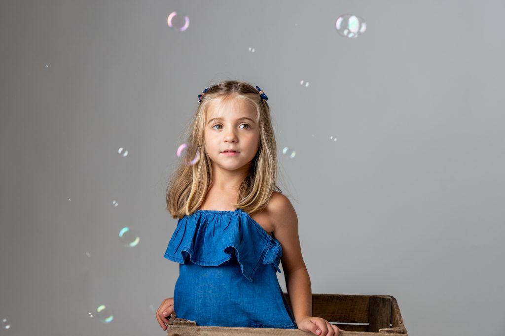 Une jeune fille, sortant d'une caisse en bois, regarde des bulles de savon s'envoler. Photo Studio Polidori