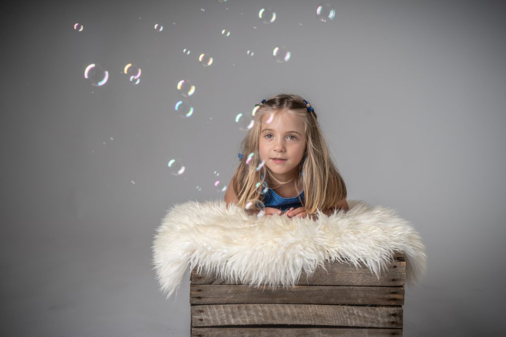 Une petite fille, reposant sur peau de mouton et caisse, rêve en regardant l'envol des bulles de savon. Photo Studio Polidori