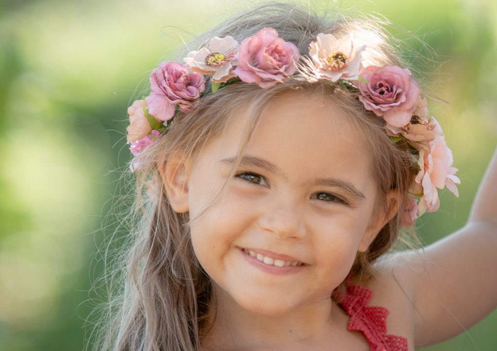 Dans la nature, une petite fille (plutôt une princesse) avec une couronne de fleurs et un beau sourire. Photo Studio Polidori