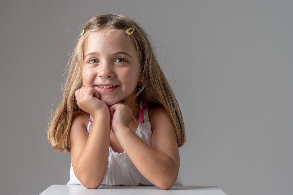 Un petite fille, tête sur les mains, jette un regard plein de malice. Photo Studio Polidori