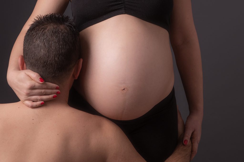 Gros plan sur ventre de femme enceinte avec la tête du papa reposant dessus. Photo Studio Polidori