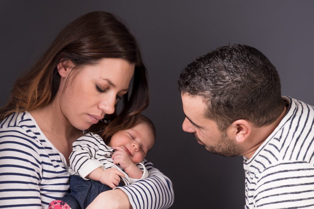 Papa et maman regarde bébé souriant. Toute la famille porte un pull marin. Photo Studio Polidori