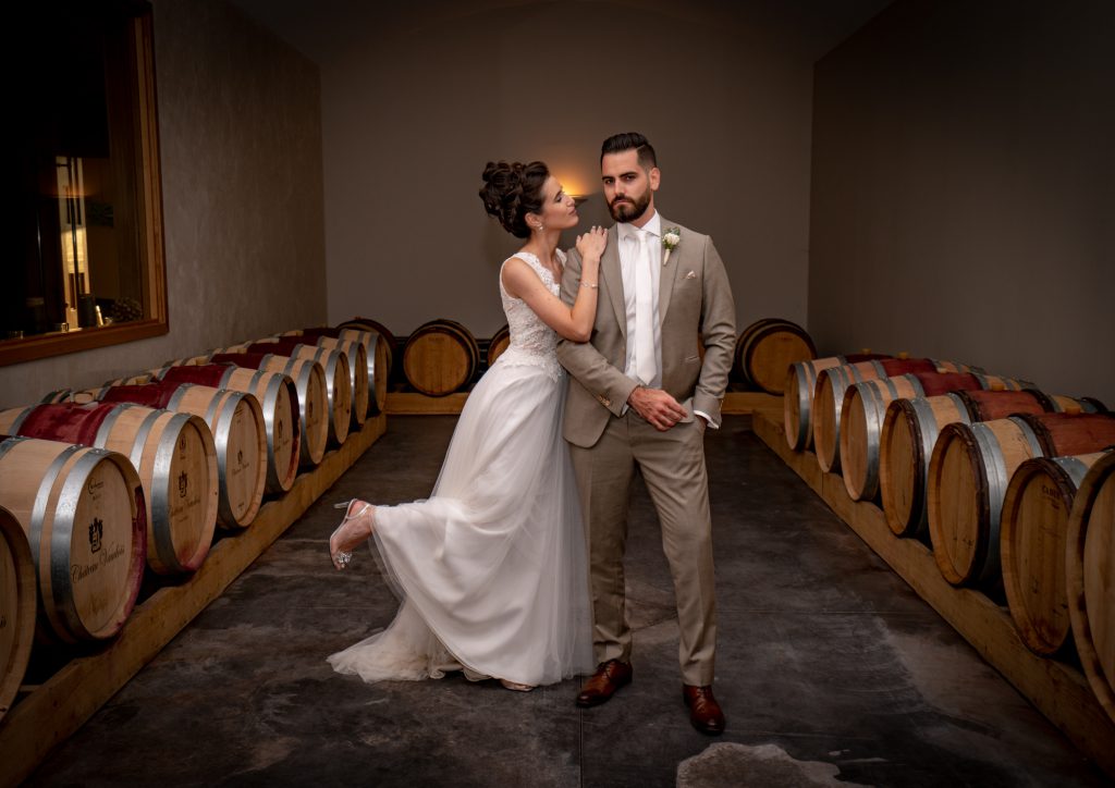 Les mariés sont devant les fûts de chêne au Château Vaudois à Roquebrune sur Argens. La mariée s'appuie tendrement sur le marié, qui reste impassible. Photo Studio Polidori