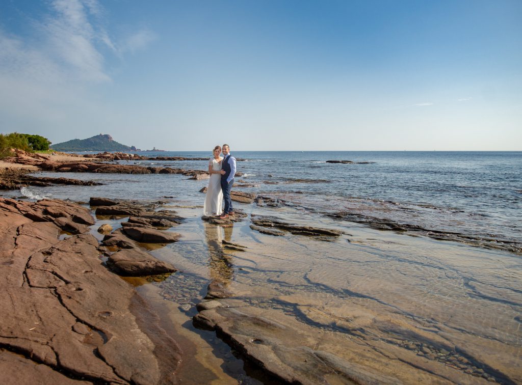 Les mariés sont dans les rochers devant la mer à Boulouris, avec l'île d'Or au fond. Photo Studio Polidori