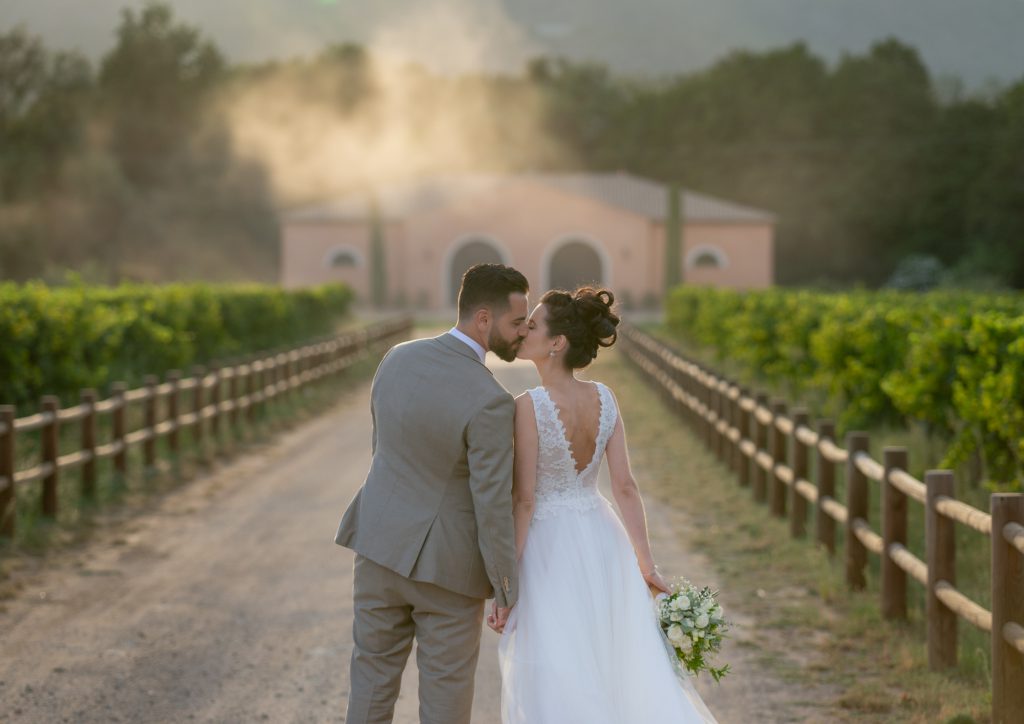 Les mariés , de dos, s'embrassent dans les vignes, avec tourbillon de sable. Au Château Vaudois à Roquebrune sur Argens. Photo Studio Polidori